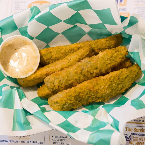 A basket of golden-brown fried pickle spears with a side of creamy dipping sauce.