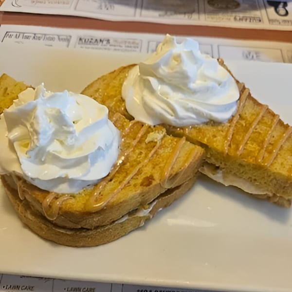 Two golden-brown French toast slices topped with whipped cream and syrup on a white plate.