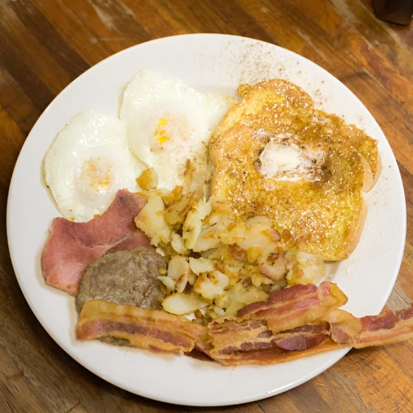 A hearty breakfast platter with French toast, eggs, bacon, sausage, and home fries.